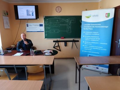 Sala wykładowa z tablicą i rolupem projektu